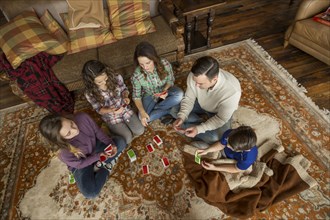 Caucasian family sitting on rug playing card game
