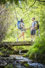 Couple carrying backpacks across bridge in woods