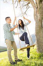 Man helping woman on tree swing