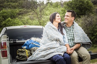 Couple wrapped in blanket sitting on bed of pick-up truck
