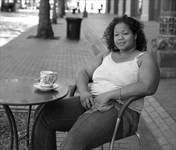 Mixed race woman drinking coffee at sidewalk cafe