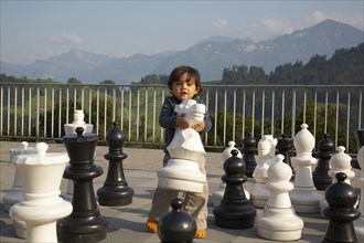 Mixed race boy playing with large chess pieces