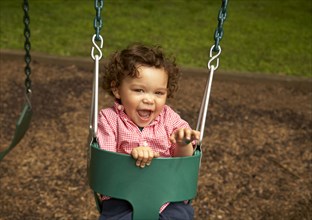 Mixed race child sitting in swing laughing