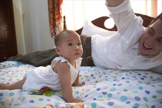 Father playing with baby girl on bed
