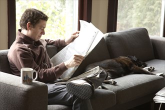 Caucasian man reading newspaper on sofa with dog
