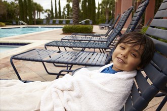 Mixed race boy reclining on lounge chair at poolside