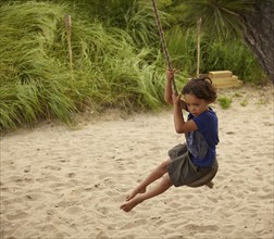 Mixed race boy playing on swing