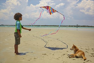 Mixed race boy flying kite on beach