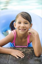 Smiling mixed race girl leaning on edge of swimming pool