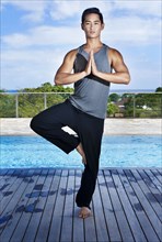 Asian man practicing yoga at poolside