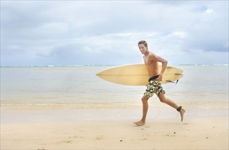 Caucasian man running on beach carrying surfboard