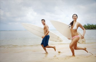 Couple running on beach carrying surfboards