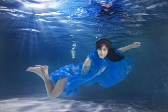 Hispanic woman swimming underwater with scarf