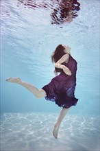 Caucasian woman in dress swimming underwater