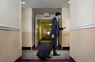 Asian businessman pulling suitcase in hotel