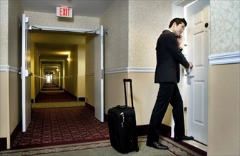 Asian businessman using cell phone and entering hotel room