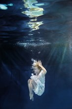 Caucasian woman in dress swimming under water