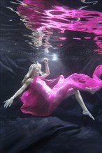 Caucasian woman in dress swimming under water