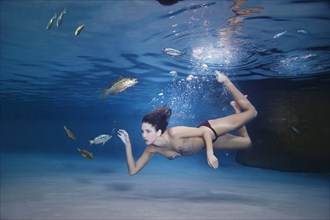 Mixed race woman swimming in water with fish