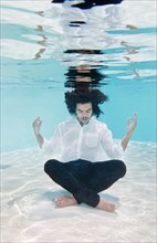 Mixed race man in clothes underwater in swimming pool