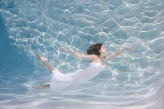 Underwater view of Caucasian woman in dress swimming in pool