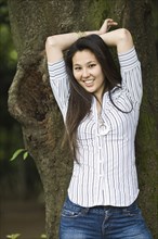 Japanese woman leaning against tree trunk