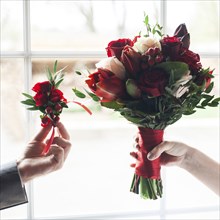 Hands of Caucasian couple holding corsage and bouquet of flowers