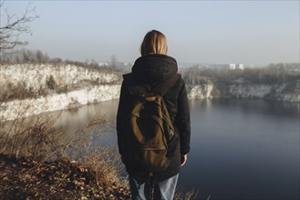 Caucasian woman standing at the edge of reservoir wearing backpack