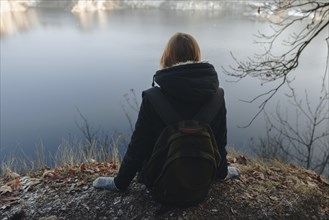 Caucasian woman sitting at the edge of reservoir wearing backpack