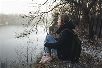 Caucasian woman sitting at the edge of reservoir wearing backpack