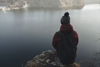 Caucasian man sitting at the edge of reservoir wearing backpack