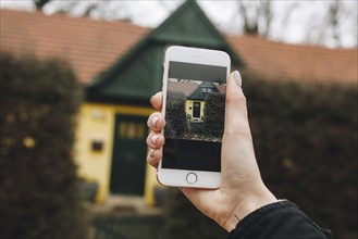 Hand of Caucasian woman photographing house with cell phone