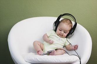Baby in chair wearing adult headphones
