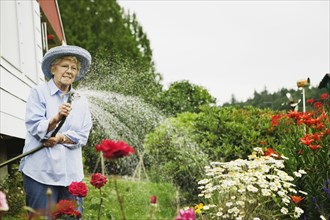 Senior woman watering plants with hose