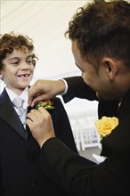 Hispanic father fastening boutonniere for son