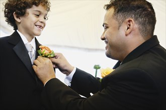 Hispanic father fastening boutonniere for son
