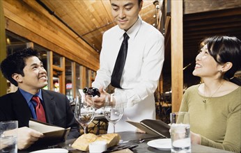Asian waiter pouring wine for customers
