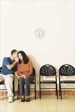 Multi-ethnic couple telling secret in waiting area