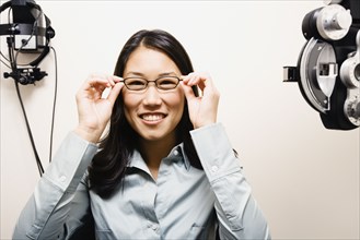 Asian woman putting on eyeglasses