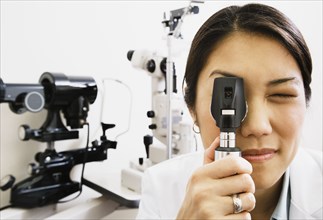 Asian female optometrist looking through equipment