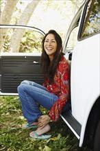 Hispanic woman sitting on side of car