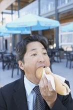 Asian businessman eating hot dog outdoors