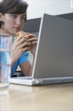 Hispanic woman looking at laptop and eating