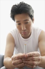 Asian man frowning at cigarette
