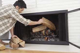 Asian man putting logs in fireplace