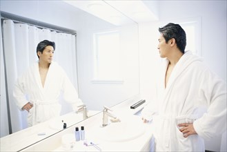 Asian man looking in bathroom mirror