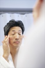 Asian man rubbing face in mirror