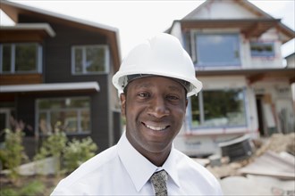 Smiling Black real estate agent in hard-hat near construction site