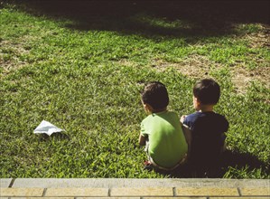 Hispanic brothers with paper airplane on lawn