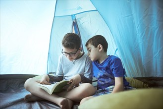 Hispanic boys camping in tent and reading book